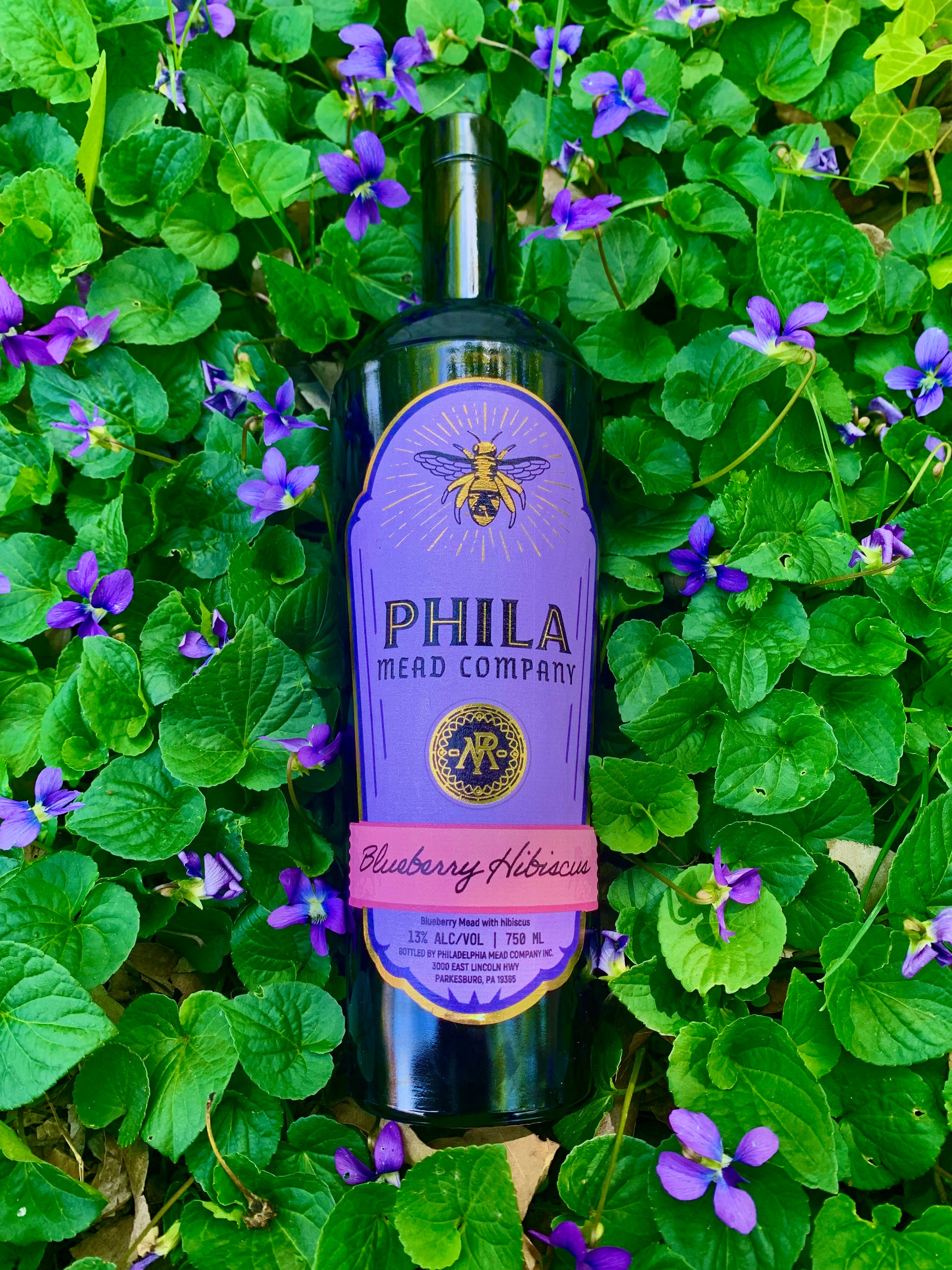 A bottle of our Blueberry Hibiscus mead, lain in a field of violets